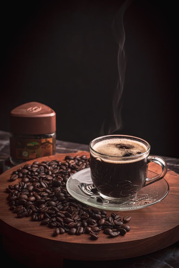 Elegant steaming coffee in glass cup with roasted beans on wooden platter, perfect for hot drink and caffeine themes.